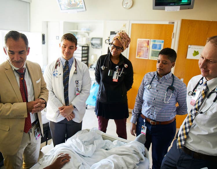 the photo depicts a care team around a patient&#39;s bed
